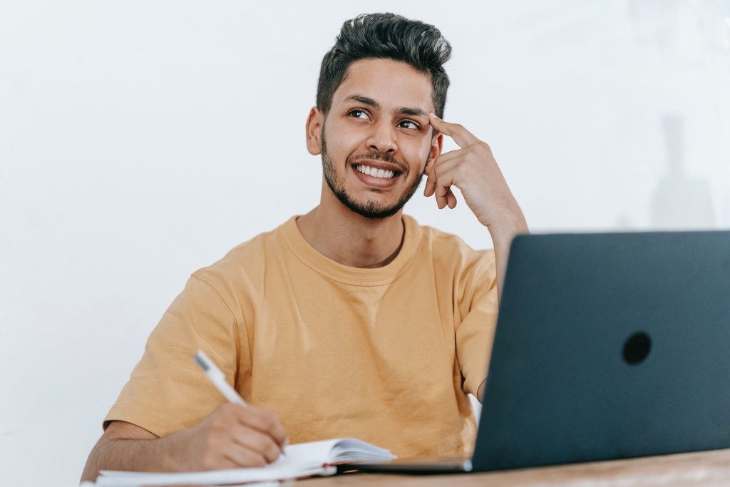 10 Best Free Cross Platform Productivity Apps In 2022.  A developer happily smiling, deep in thought with a pen poised over a paper notebook.